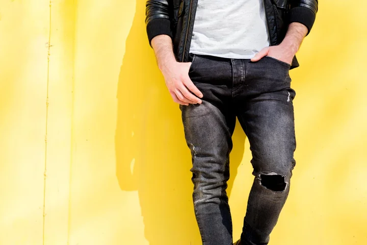 Model w czarnych jeansach męskich na żółtym tle