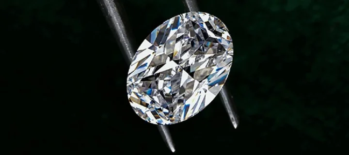 Owalny szlifowany diament trzymany pęsetą na ciemnym tle